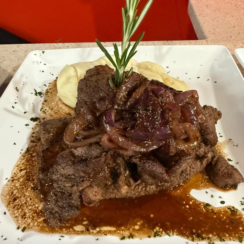 Latin-American steak with caramelized onions, mashed potatoes, and rosemary on a white plate.