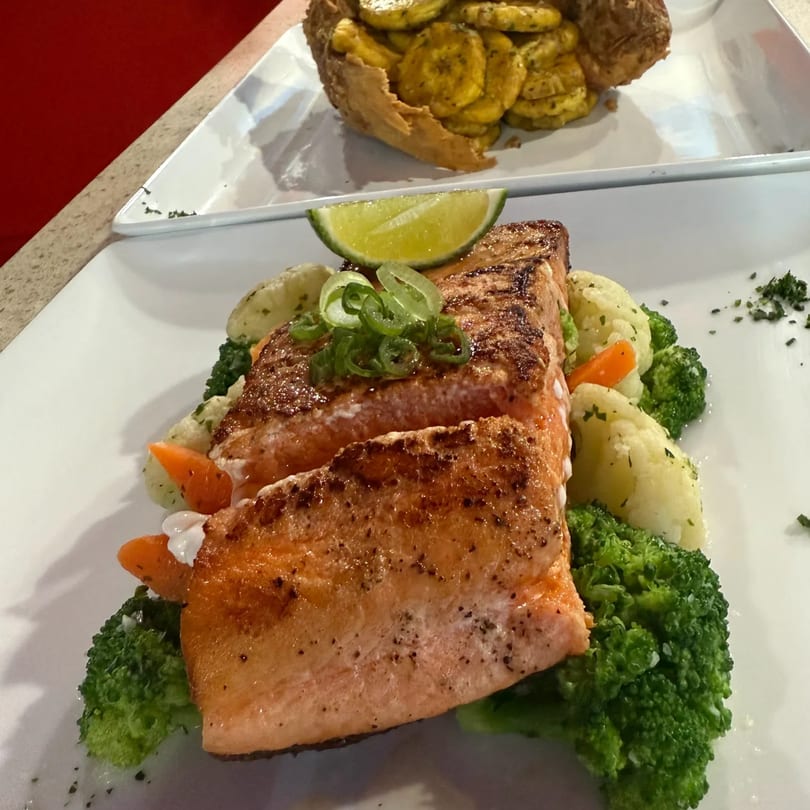 Grilled salmon with broccoli, potatoes, carrots, lime, and plantains in a basket.