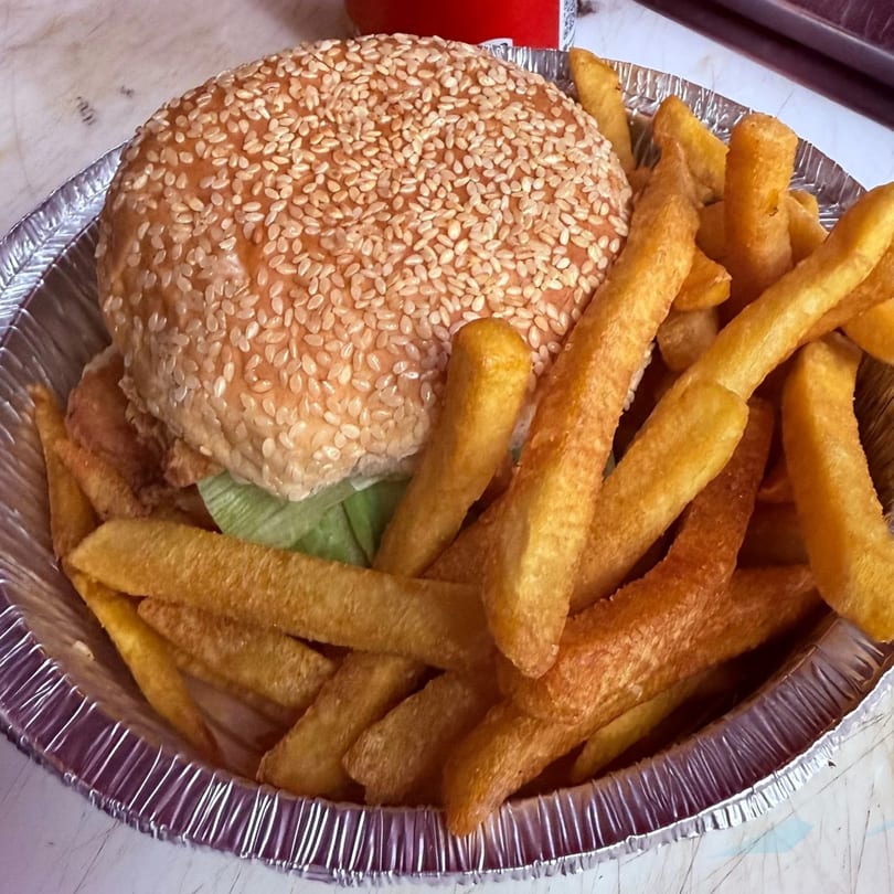 A sesame seed bun burger with lettuce and fries in a foil container from Angiolina's Restaurant.